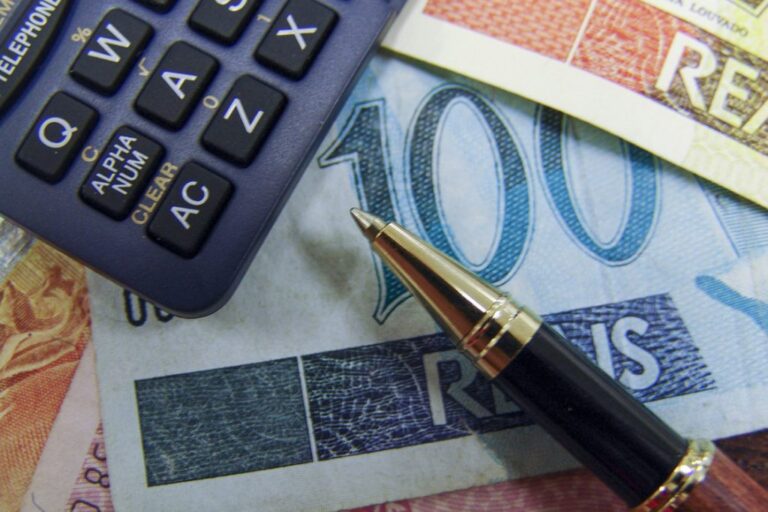 Imagem de uma nota de R$100 , uma caneta e uma calculadora