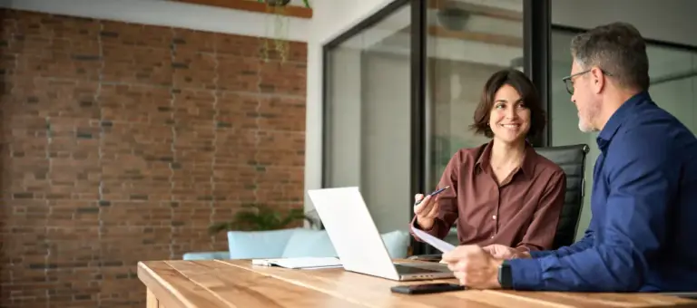 Mulher sorridente com notebook conversa com cliente em reunião de escritório para negociar uma operação de factoring