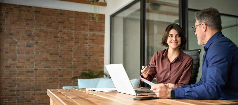 Mulher sorridente com notebook conversa com cliente em reunião de escritório para negociar uma operação de factoring