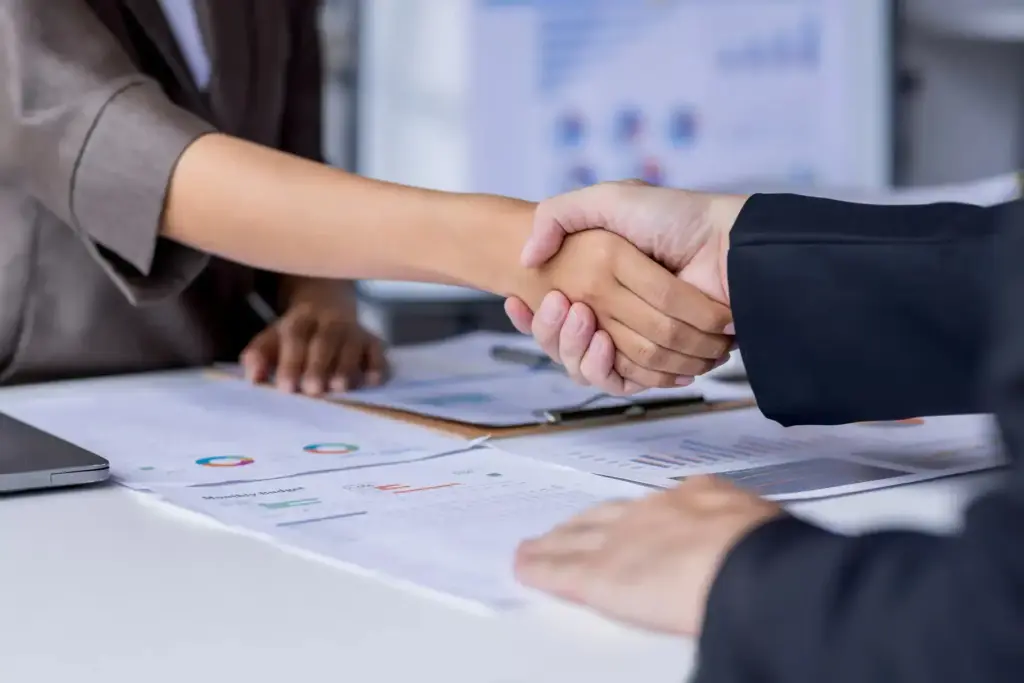 Aperto de mãos entre duas pessoas durante reunião, simbolizando acordo e negociação em processo de cobrança extrajudicial.