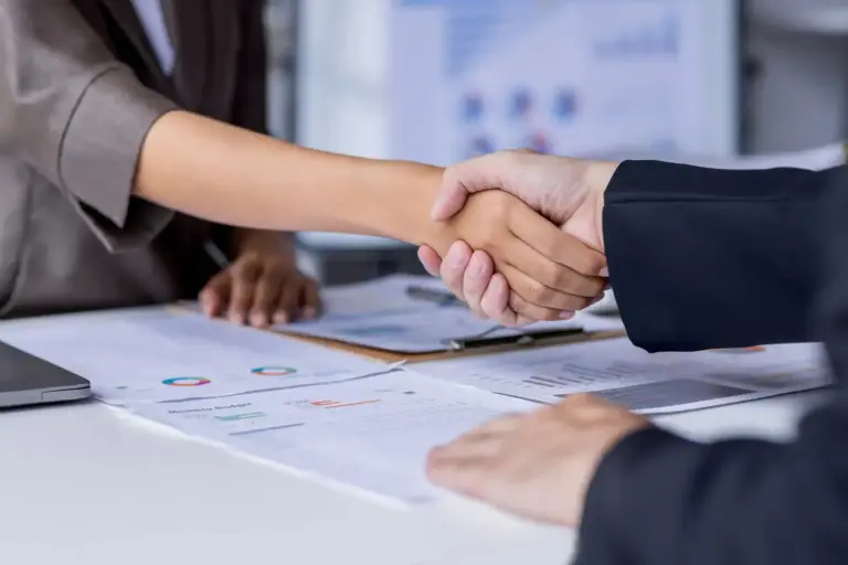 Aperto de mãos entre duas pessoas durante reunião, simbolizando acordo e negociação em processo de cobrança extrajudicial.