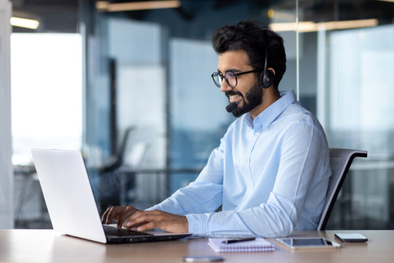 Homem usando um computador, fones e um celular.