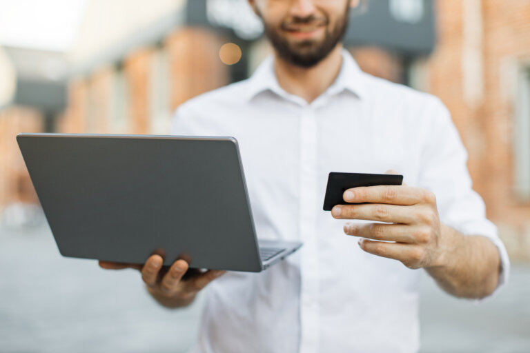 Homem com um notebook e um cartão nas mãos.