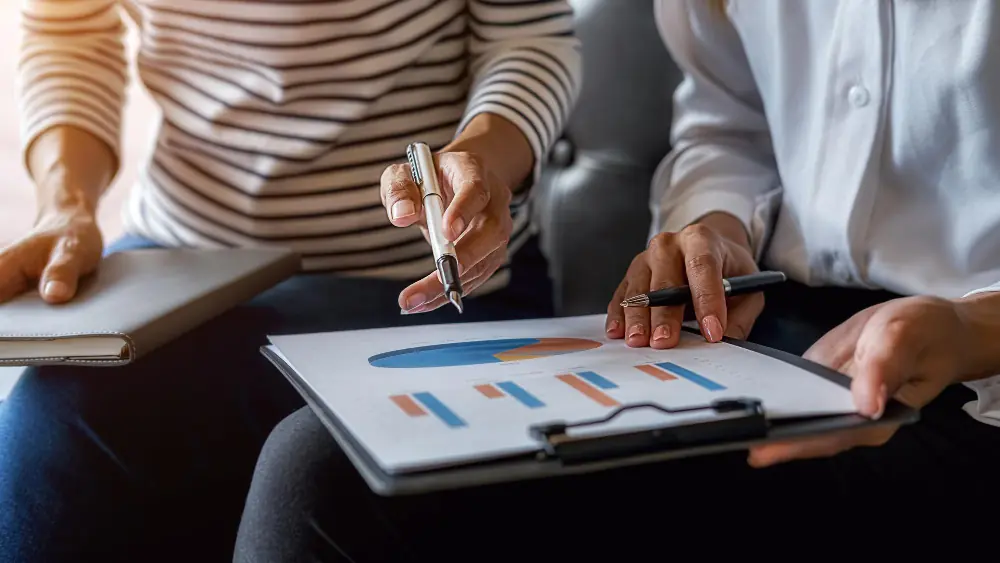 Profissionais analisando gráficos financeiros em prancheta, representando como avaliar uma empresa de forma estratégica.