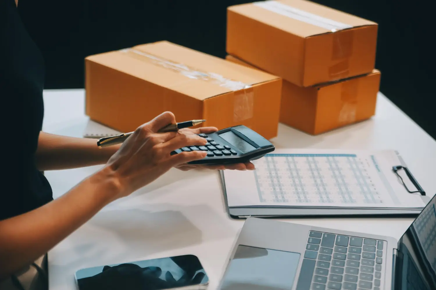 Profissional usando calculadora com caixas e planilha ao fundo representando emissão de duplicata mercantil