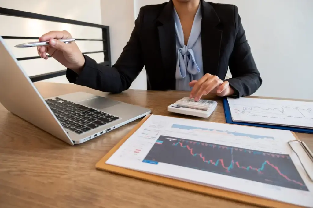 Profissional de finanças usando calculadora com gráficos e notebook sobre mesa ilustrando lastro financeiro