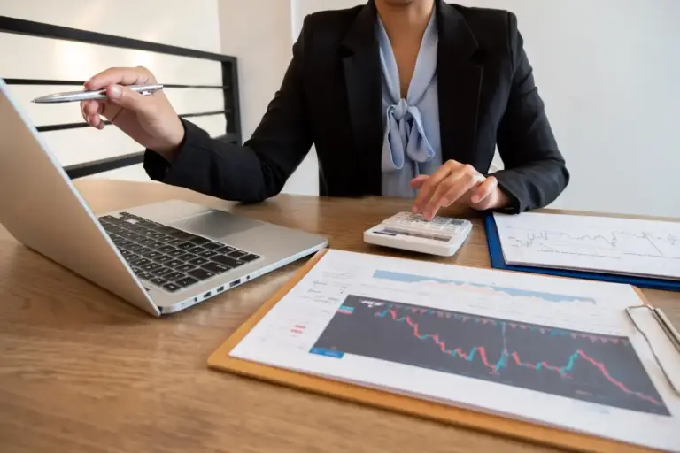 Profissional de finanças usando calculadora com gráficos e notebook sobre mesa ilustrando lastro financeiro