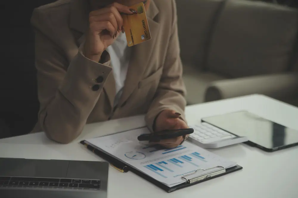 Cobrança indevida: o que fazer? Mulher verificando cartão de crédito e conferindo gráficos financeiros para identificar cobrança indevida