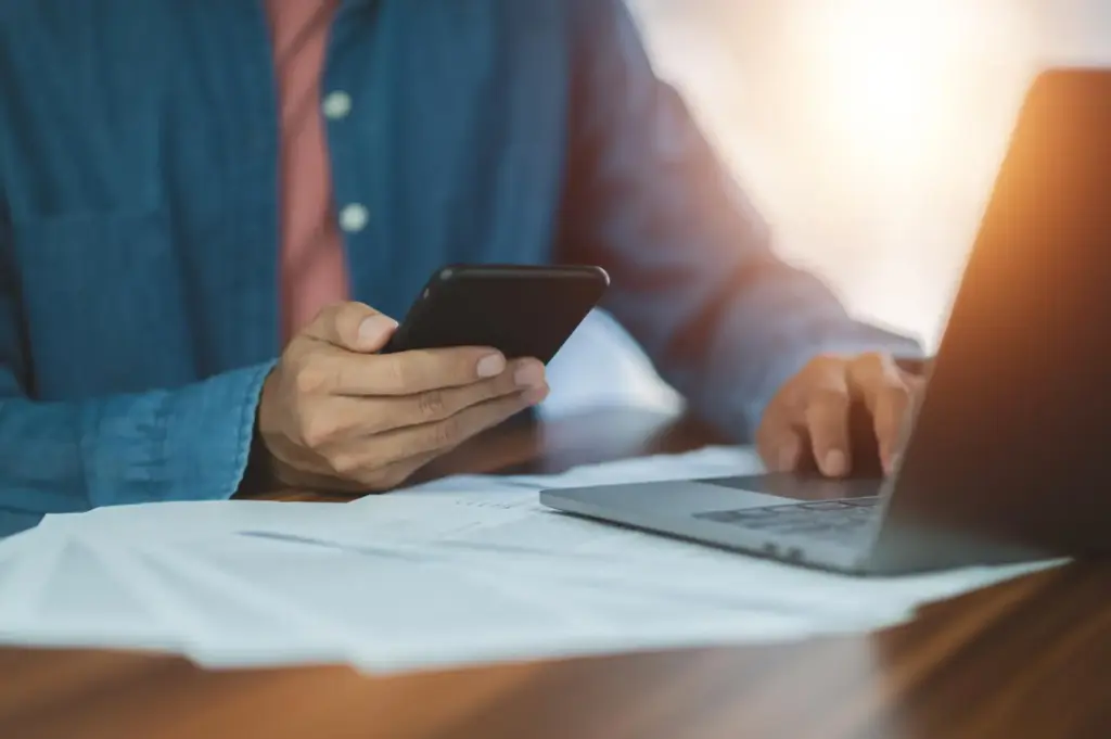 Empresário usando celular e laptop com boletos na mesa para fazer antecipação de recebíveis