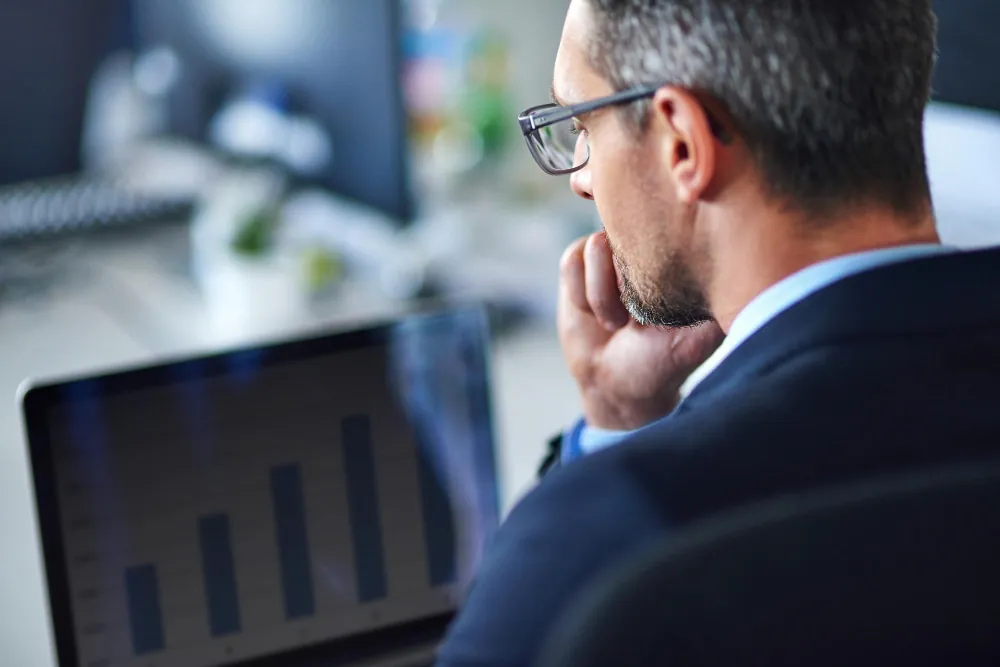 Como investir em debêntures? Executivo de terno analisando gráfico de barras em notebook, avaliando a rentabilidade de debêntures