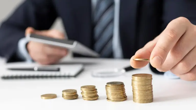 Mãos empilhando moedas em pilhas crescentes sobre mesa com calculadora e caderno, representando o rendimento de debêntures