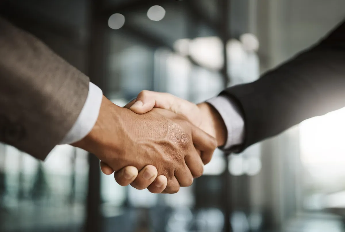 Close de aperto de mãos entre dois executivos de terno, simbolizando o acordo formalizado por meio de uma conta escrow